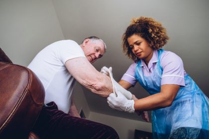 Caregiving Nurse putting a bandage on a senior mans arm in his home.